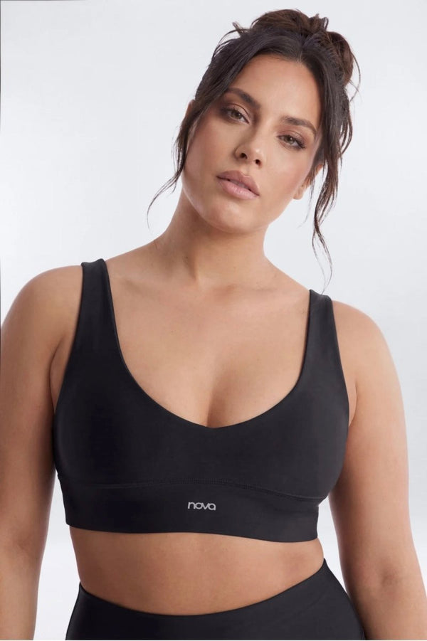 A woman wearing a black sports bra with a wide underband and a small white 'nova' logo on the front, photographed against a light gray studio background.