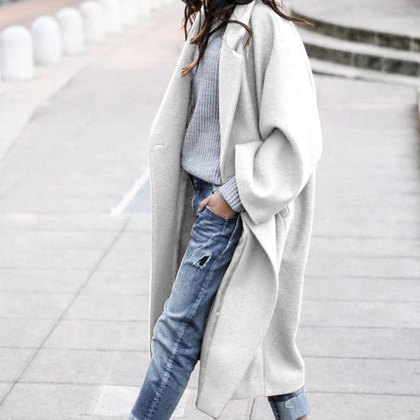 Person wearing a long white coat over a light blue sweater and jeans on a blurred background