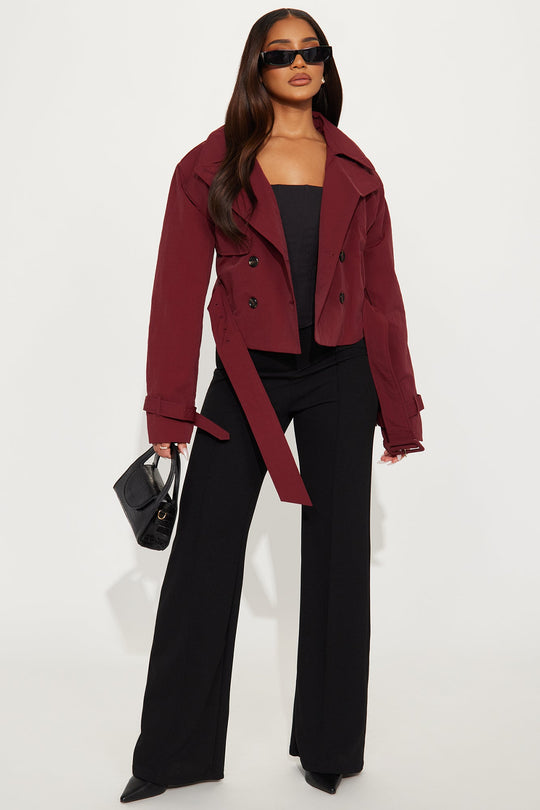 Woman wearing a burgundy coat, black top, and pants on a white background