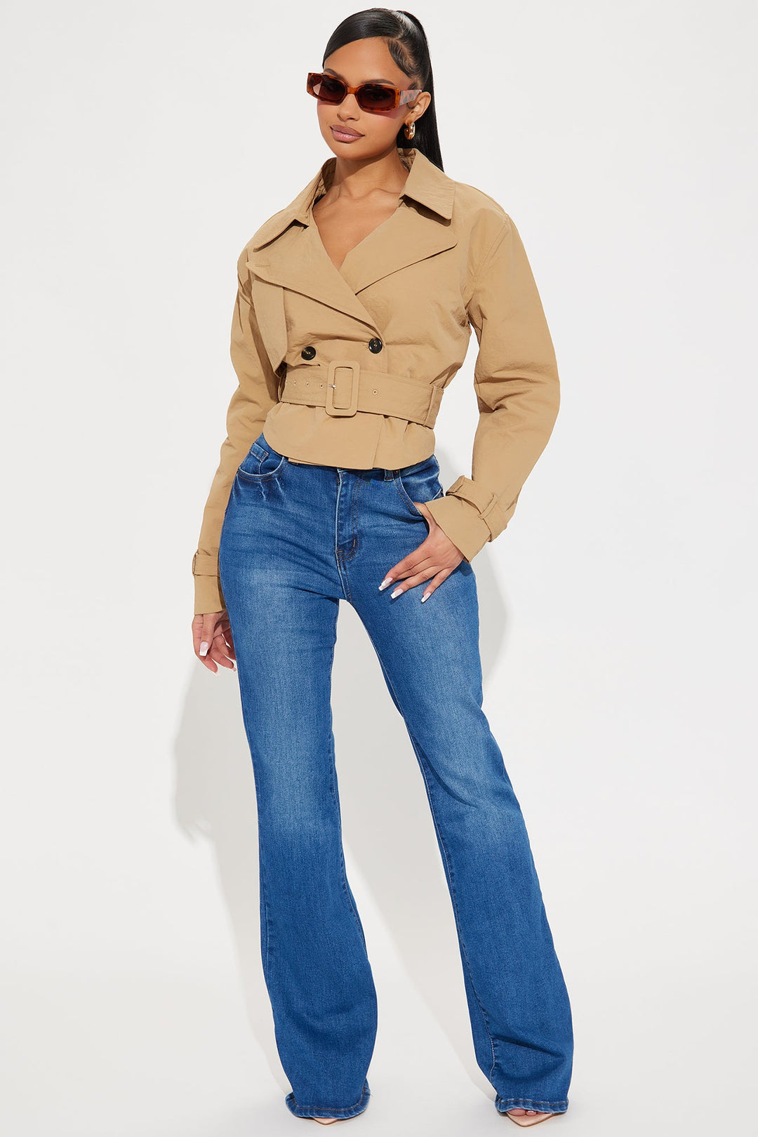 Woman wearing a beige trench coat and blue jeans on a white background