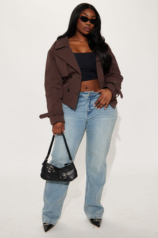 Woman wearing a brown jacket, black top, blue jeans, and holding a black handbag on a white background