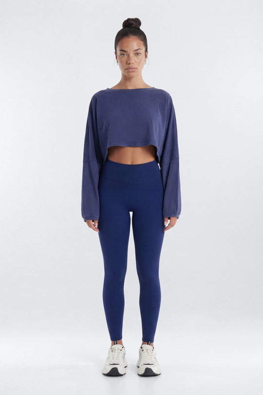 Person wearing a blue long-sleeve crop top and leggings on a white background