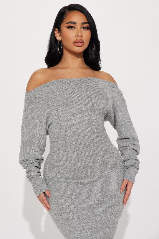Woman wearing a gray off-shoulder knit dress against a white background