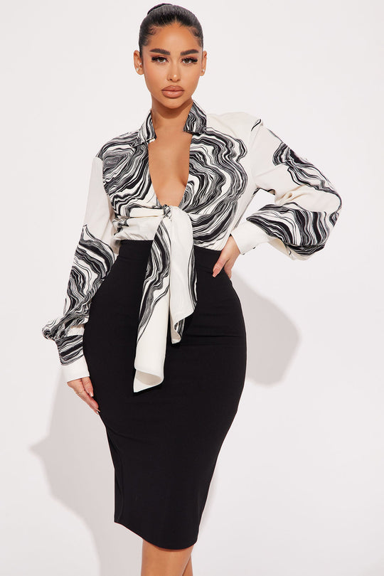 Woman wearing a black and white patterned blouse with a black pencil skirt on a white background
