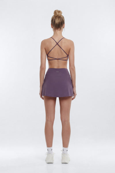 A woman stands with her back to the camera wearing a purple athletic set consisting of a strappy sports bra