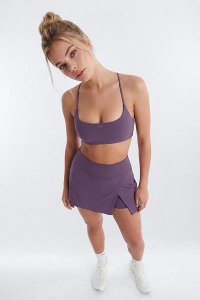 Woman wearing a purple sports bra and skirt set on a white background
