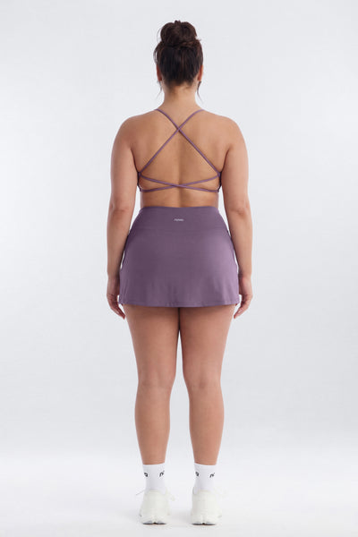Person wearing a purple athletic outfit with a strappy top on a white background