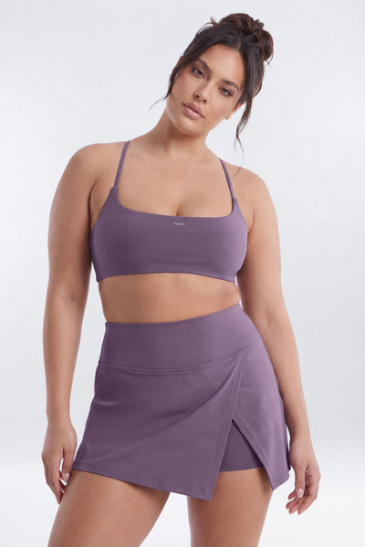 A woman modeling a matching two-piece activewear set in a dusty purple color, featuring a sports bra