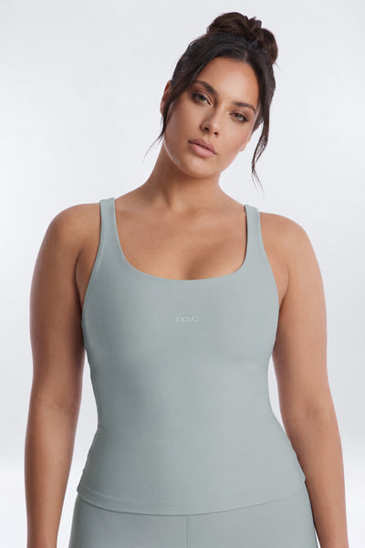 Woman wearing a light gray tank top with a brand logo on a white background
