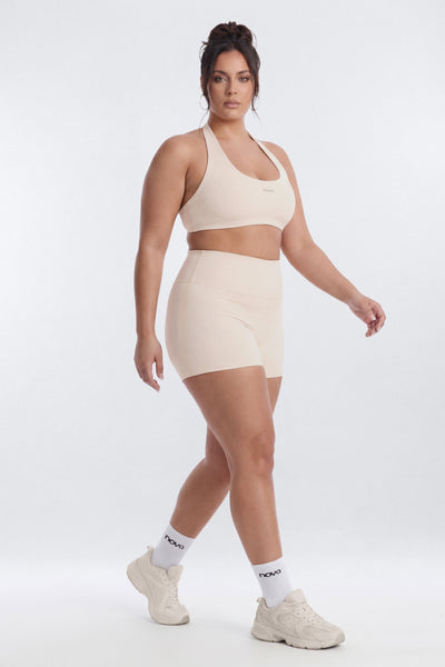 Woman wearing a beige sports bra and shorts set on a white background
