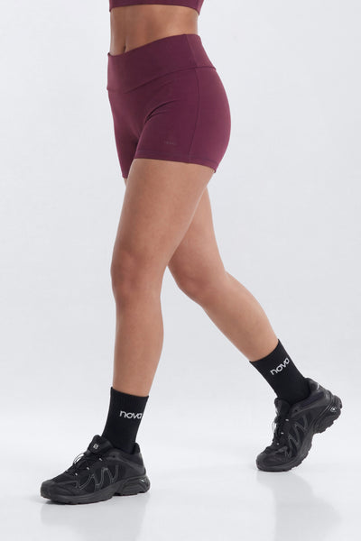 Person wearing maroon athletic shorts and black sneakers on a white background