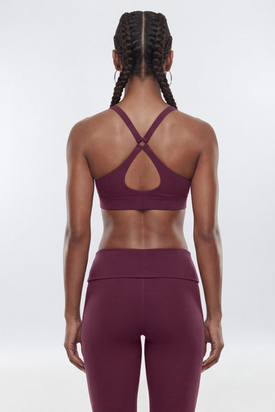 A woman modeling a matching burgundy activewear set consisting of a sports bra with a high-waisted leggings