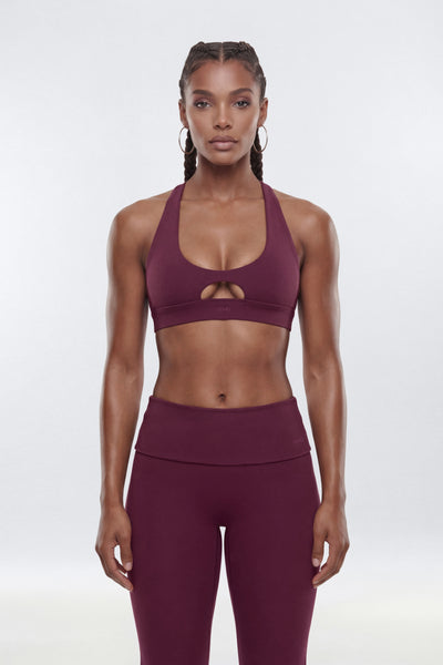 A woman modeling a matching burgundy activewear set consisting of a sports bra with a keyhole cutout and high-waisted leggings