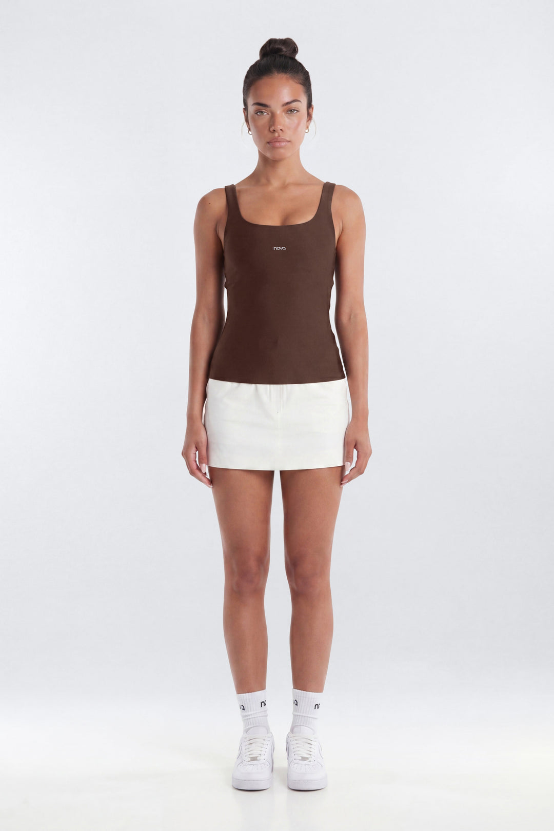 Woman wearing a brown tank top and white shorts on a white background