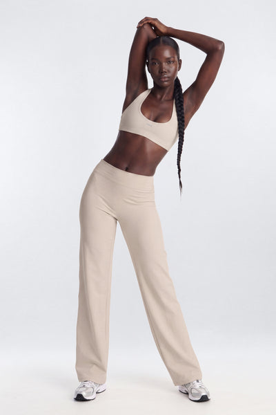 Woman wearing a beige sports bra and pants on a white background