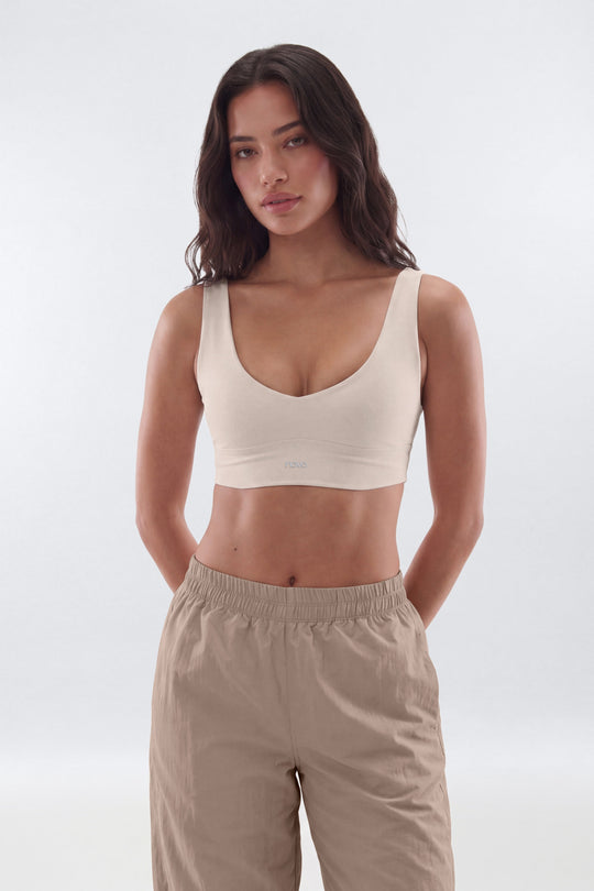 A woman modeling a beige scoop-neck crop top and beige drawstring pants against a light gray studio background.