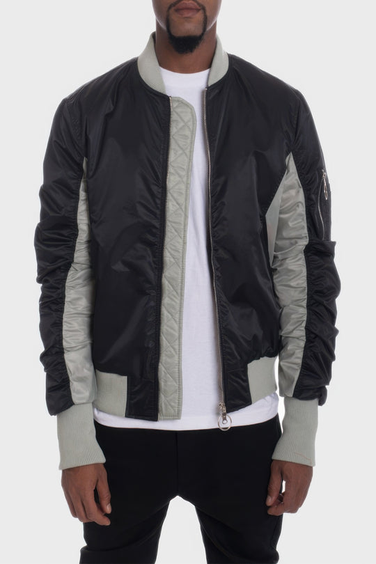 Person wearing a black and gray jacket with a white shirt underneath on a light gray background