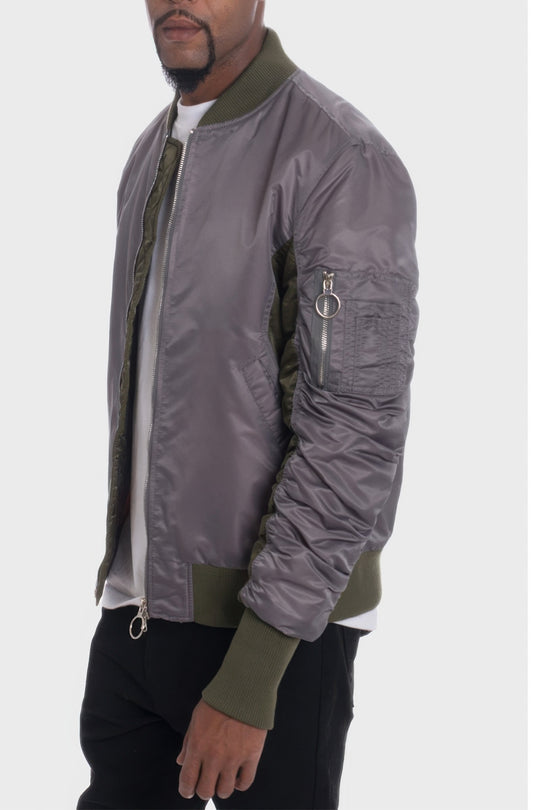Person wearing a gray bomber jacket with green accents on a white background