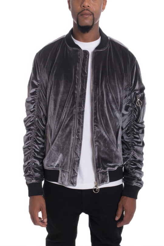 Man wearing a gray velvet bomber jacket over a white shirt on a white background