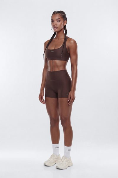 Woman wearing a brown sports bra and shorts set on a white background