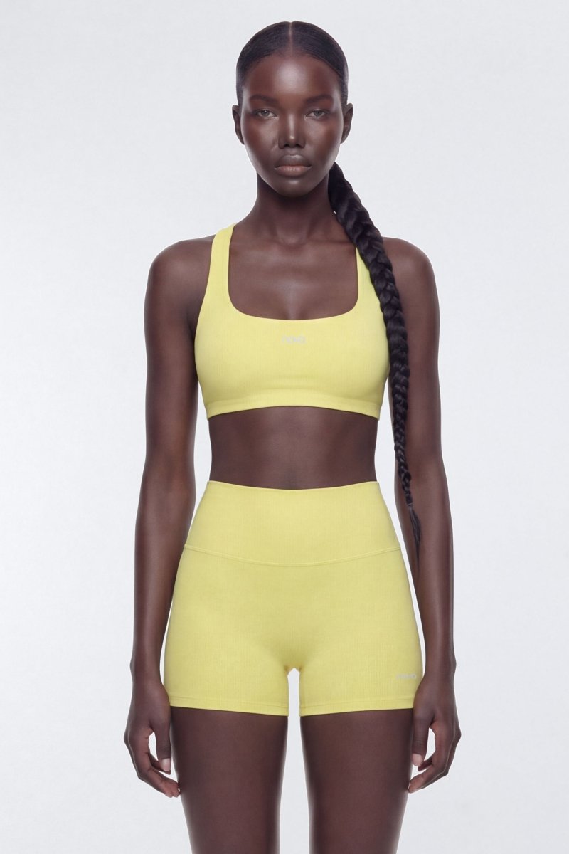 Model wearing a yellow sports bra and shorts set on a white background