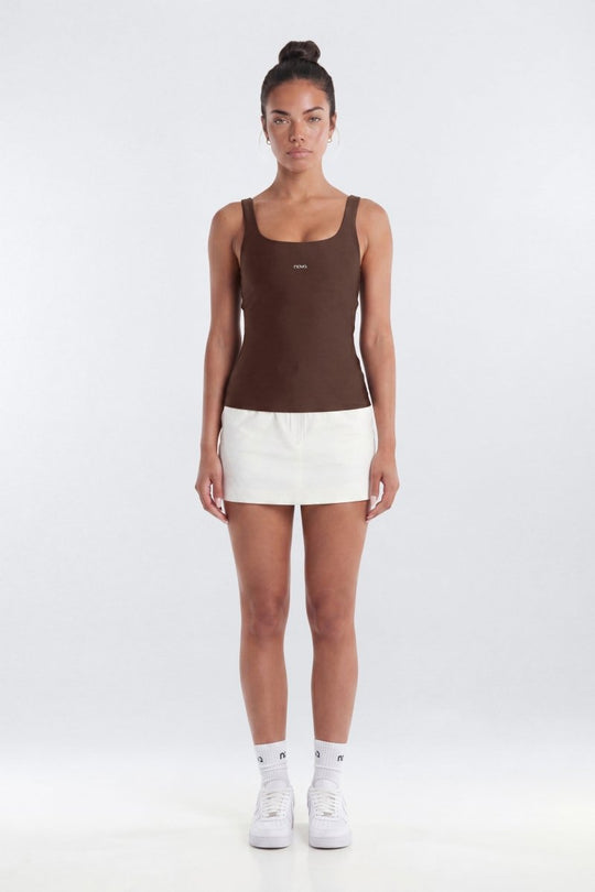 Woman wearing a brown tank top and white shorts on a white background