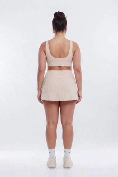 Person wearing a beige sports bra and skirt set on a white background