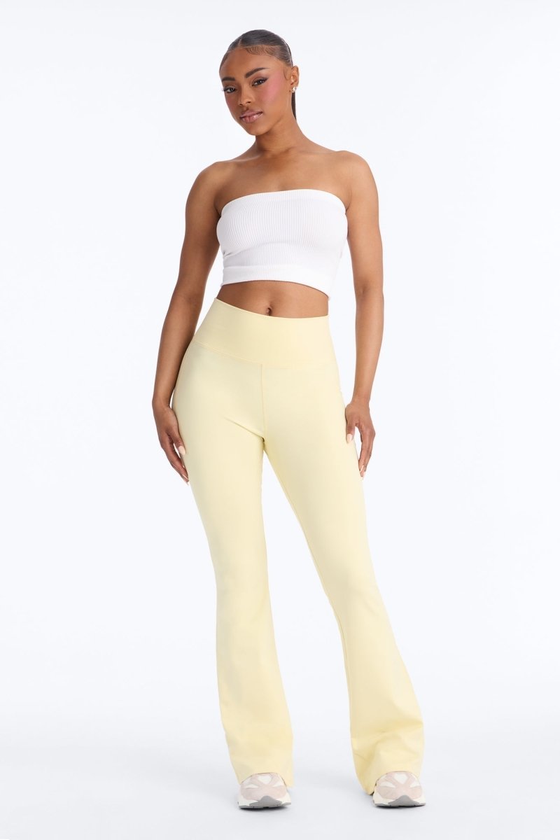 Woman wearing a white strapless top and yellow pants on a white background