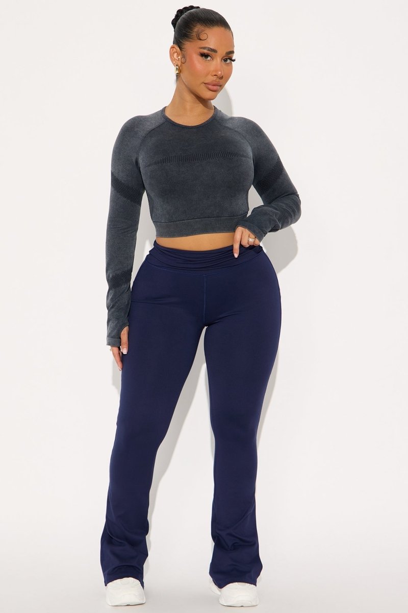 A woman modeling a dark gray long-sleeve crop top and navy blue high-waisted flared sweatpants against a plain white studio background.
