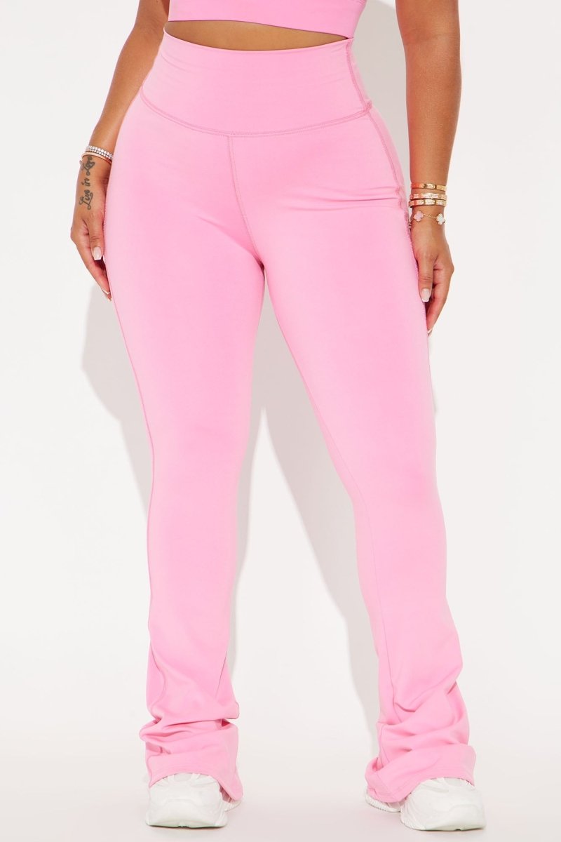 A person wearing bright pink high-waisted flared leggings with ruched side details and white sneakers, shown from the torso down against a plain light background.