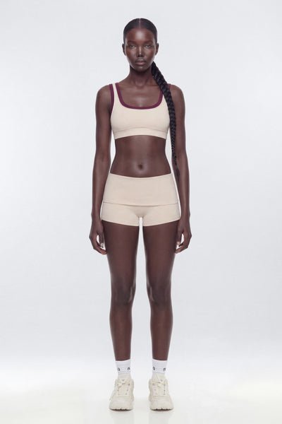 Woman wearing a beige sports bra and shorts set on a white background