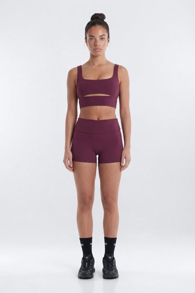 Woman wearing a maroon sports bra and shorts set on a white background