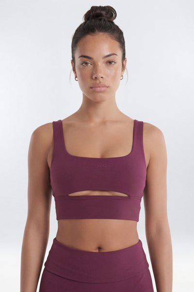 A woman modeling a matching athletic set featuring a scoop-neck crop top with a horizontal chest cutout and high-waisted leggings.