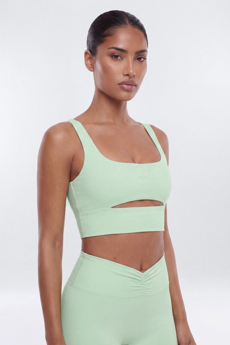 Woman wearing a light green sports bra and leggings on a white background