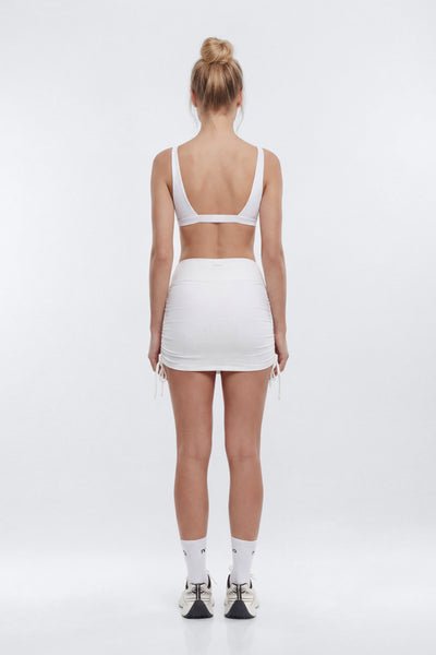 Person wearing a white sports bra and skirt set on a white background