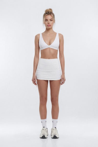 Woman wearing a white sports bra and skirt set on a white background