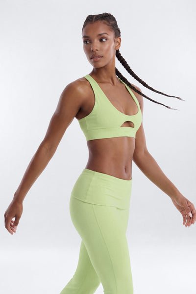 Woman wearing a green sports bra and leggings on a white background