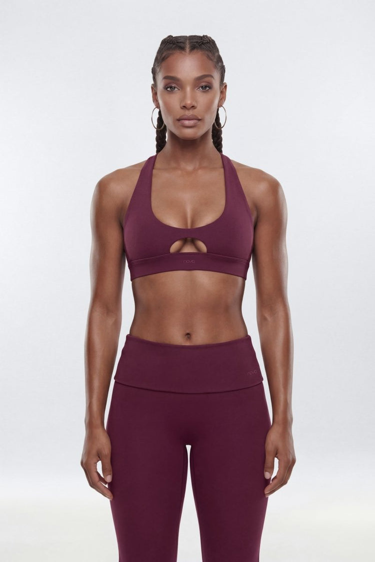 A woman modeling a matching athletic set consisting of a deep plum purple sports bra with a keyhole cutout and high-waisted leggings.