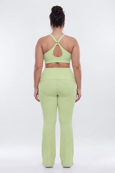 A woman viewed from the back wearing a light lime green matching activewear set consisting of a sports bra with an open back and high-waisted flared leggings, set against a plain white studio background.