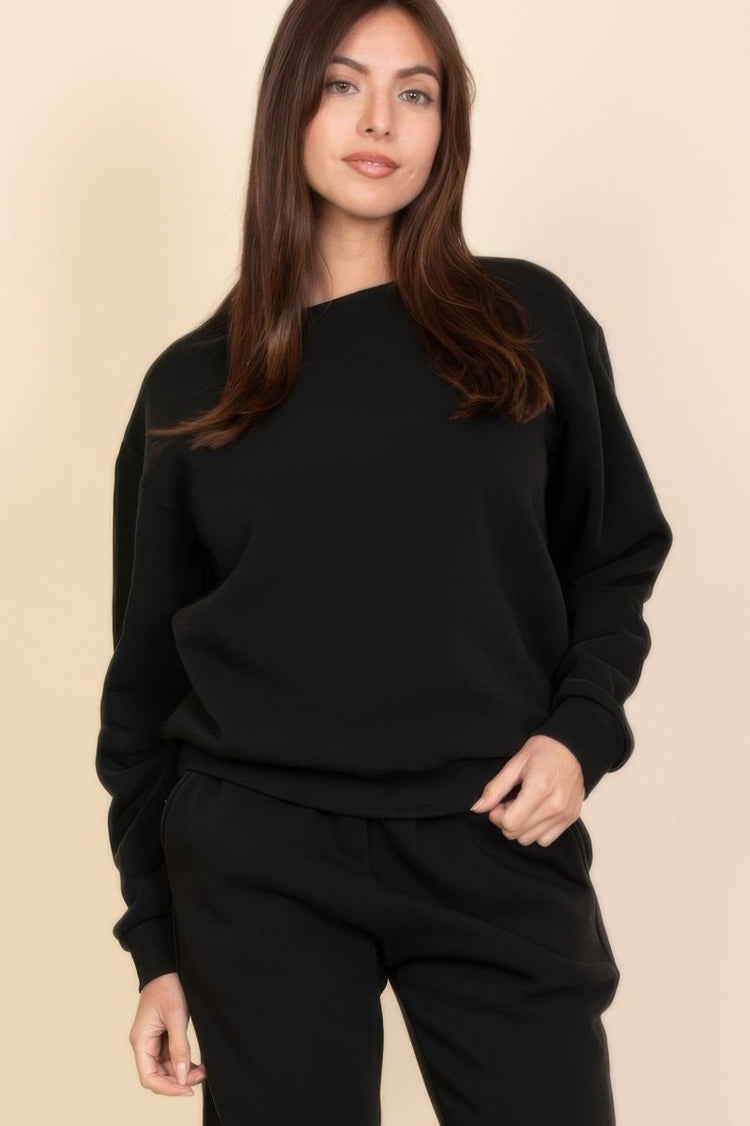 Woman wearing a black sweater and pants against a beige background