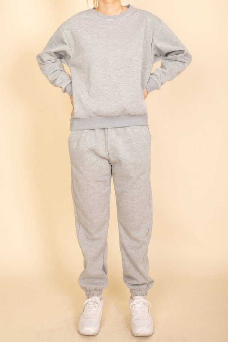 Person wearing a gray sweatshirt and pants set with white sneakers on a beige background