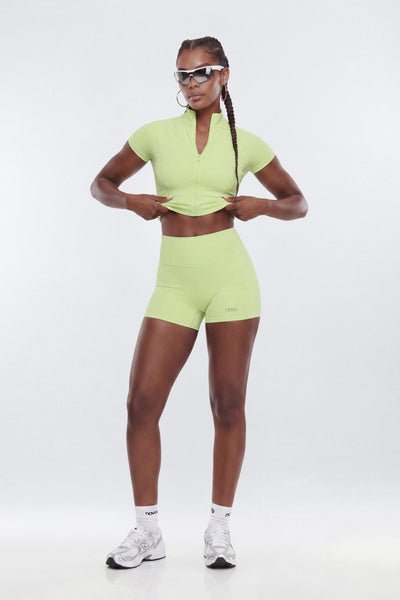 A model wearing a matching lime green athletic set consisting of a short-sleeve crop top with a split neckline and high-waisted shorts.