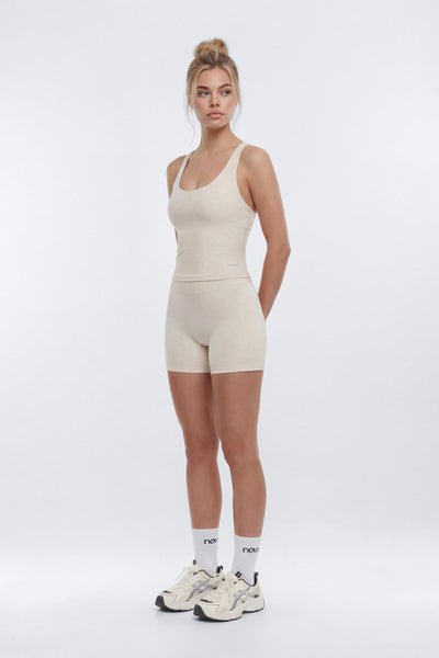 A woman modeling a light beige ribbed tank top and matching high-waisted shorts set, paired with white socks and chunky white sneakers, against a plain light gray studio background.