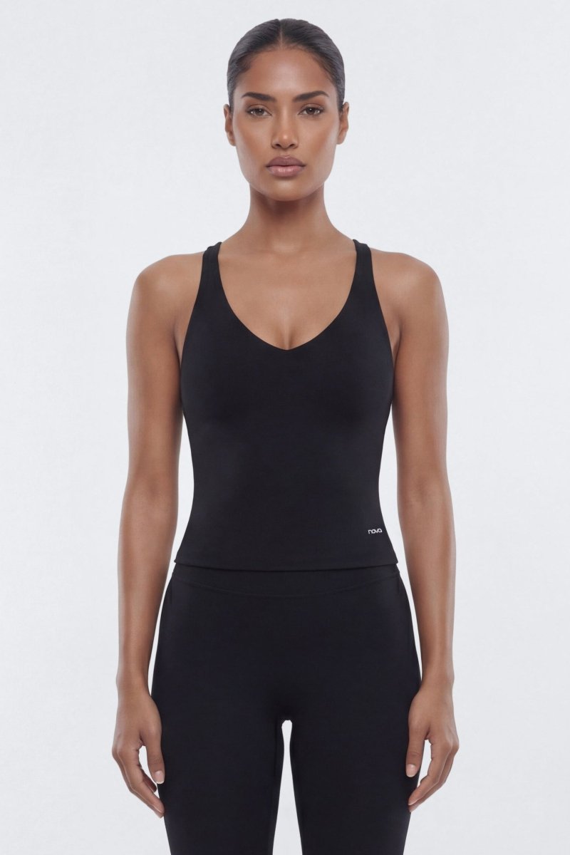 A woman modeling a black sleeveless scoop-neck bodysuit or jumpsuit with matching black leggings against a plain light gray studio background.