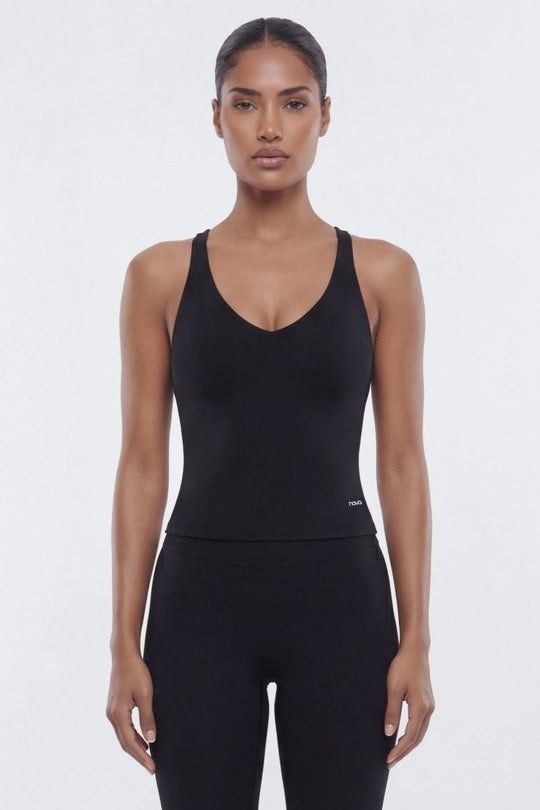 A woman modeling a black sleeveless scoop-neck bodysuit or jumpsuit with matching black leggings against a plain light gray studio background.