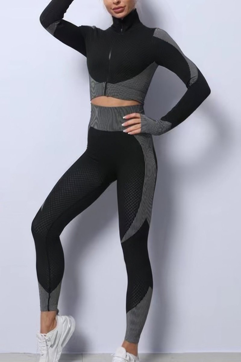 A woman modeling a matching black and gray long-sleeve athletic crop top and high-waisted leggings set with textured knit panels, posed against a light gray studio wall.