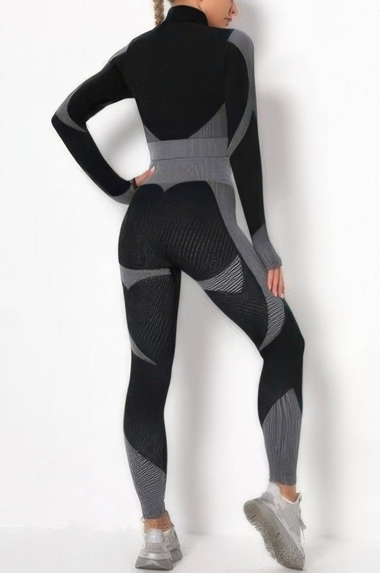 A woman modeling a black and gray long-sleeve athletic jumpsuit from the back, wearing gray sneakers, against a plain white studio background.