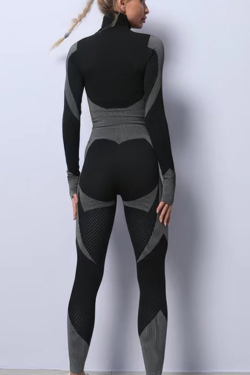 A woman shown from the back wearing a fitted long-sleeve one-piece bodysuit or tights in black with gray contrast panels and textured knit sections, standing against a plain light gray wall.