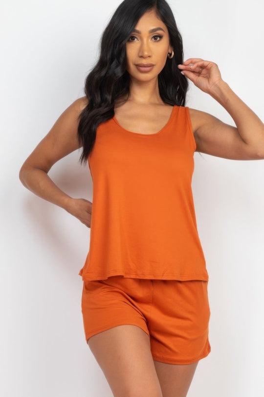 Woman wearing an orange sleeveless top and shorts on a white background