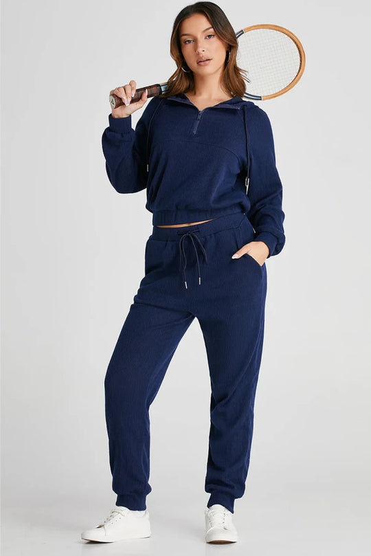 Woman wearing a navy tracksuit holding a tennis racket on a white background